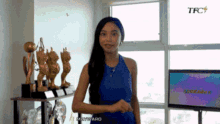 a woman in a blue dress is standing in front of trophies and a tfc sign