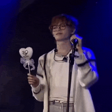 a man wearing glasses is holding a heart shaped lollipop in front of a microphone .
