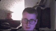 a young man wearing glasses and ear buds is sitting in front of a computer screen .