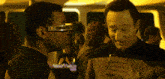 a man wearing a pair of futuristic glasses talks to another man holding a glass