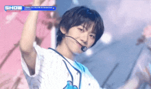 a young man wearing a baseball uniform and a microphone is dancing on stage .