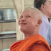 a bald man wearing an orange robe is smiling while sitting next to another man .