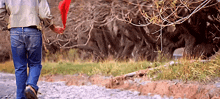 a man is walking down a dirt path holding a red feather