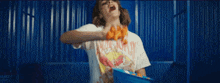 a woman in a white t-shirt is standing in front of a blue wall holding a blue bucket .