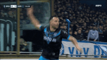 a soccer player in a black and blue jersey celebrates a goal against her