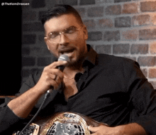 a man in a black shirt is singing into a microphone while holding a championship belt