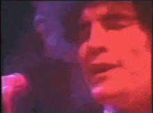 a close up of a person singing into a microphone with a pink and purple background .