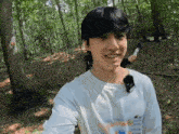 a young man in a white shirt is standing in the woods smiling