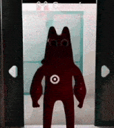 a red gummy bear with a target on its chest is standing in front of a door .