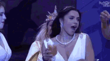 a woman in a white dress is holding a glass of wine while standing next to another woman .