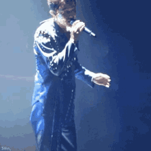 a man in a blue jacket is singing into a microphone on stage .