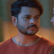 a man with a beard and a red shirt is looking at another man