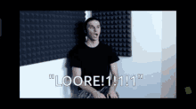 a man in a black shirt is sitting in front of a wall that says loore