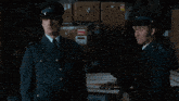 two men in military uniforms are talking in a dark room with boxes in the background
