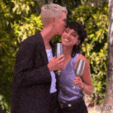 a woman kisses another woman on the cheek while holding a glass