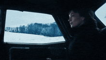 a woman in a car looking out the window at the snow