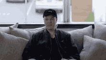 a man wearing a black hat and a black jacket is sitting on a couch near a window