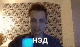 a man is holding a cell phone in front of a wall with a patterned curtain behind him