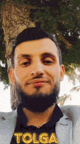 a man with a beard is standing in front of a tree and has the name tolga on his shirt