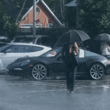 a woman walking in the rain with an umbrella in front of a black sports car