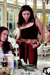 a woman in a black crop top and red pants is standing next to a table with a bowl of food .