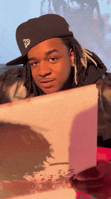 a man with dreadlocks wearing a new era hat looks at something