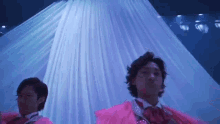 two men in pink dresses are dancing on a stage in front of a white curtain .