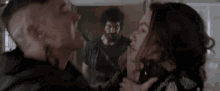 a man is holding a woman 's neck in a room while another man watches .