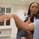 a woman in a bra and denim vest is dancing in a room .