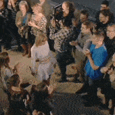 a woman in a white dress stands in a crowd of people while a man takes a picture of her