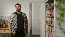 a man in a black and white checkered shirt stands in front of a wall that has the word friend written on it