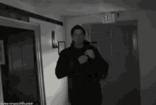 a man in a black jacket is standing in a hallway .