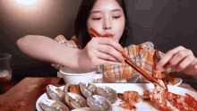 a woman is eating a plate of seafood with chopsticks