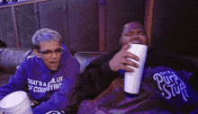 two men sitting on a couch one wearing a shirt that says purple stuff