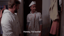 a man in a bloody shirt is standing next to another man and says honey i 'm home