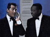 two men in tuxedos are standing next to each other talking on a phone .