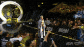 a wrestler is walking down a stage with a crowd behind him and the word aew on the wall