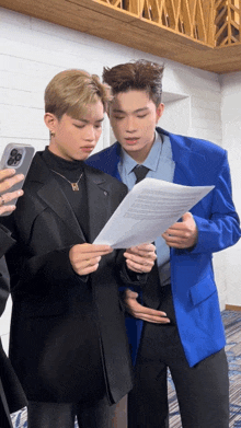 a man in a blue jacket holds a piece of paper next to another man in a black suit