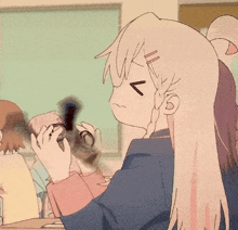 a girl with long blonde hair is sitting at a table with a cat in her hand
