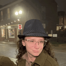 a woman wearing a hat and glasses is smiling in front of a no parking sign