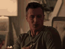 a man in a green shirt is sitting on a couch with a lamp in the background