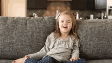 a little girl is sitting on a couch laughing and smiling .