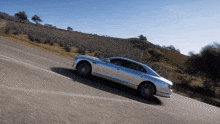 a silver car is driving down a road with a field in the background