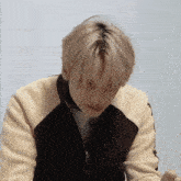 a young man with blonde hair is wearing a black and white sweater and looking down .