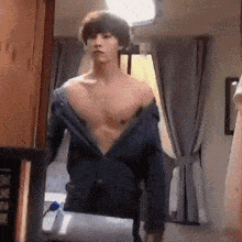 a shirtless man is standing in front of a mirror taking off his jacket .