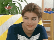 a woman in a blue shirt is sitting on a yellow and white striped couch and smiling .
