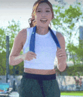 a woman in a white tank top and green shorts is running with a blue towel around her neck