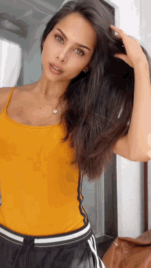 a woman in a yellow tank top and black shorts holds her hair