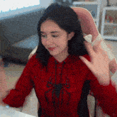 a woman wearing a red spider man hoodie is sitting in a chair