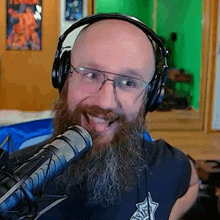 a bald man with a beard and glasses is wearing headphones and talking into a microphone .